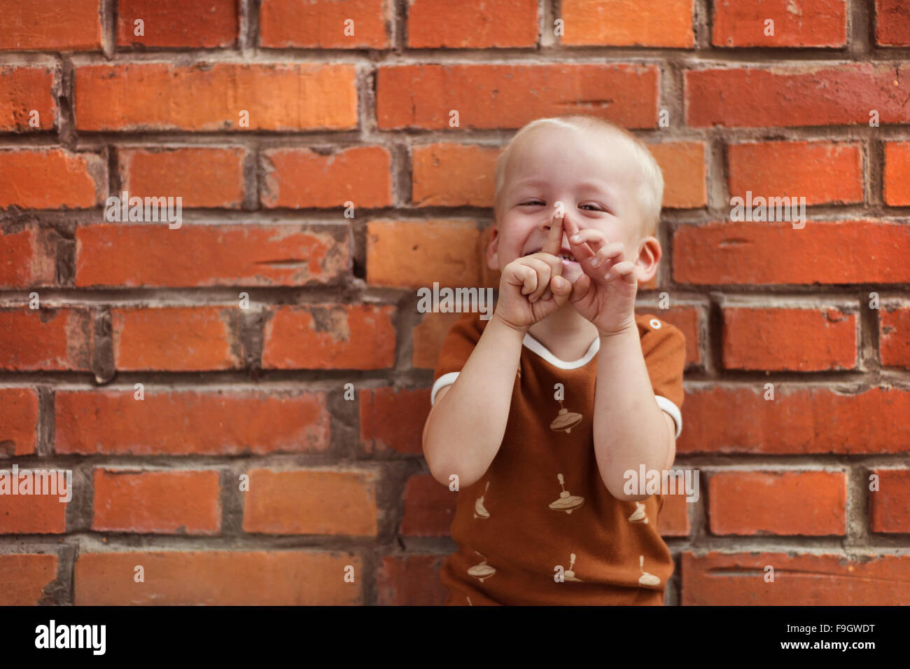 Cute little boy making funny faces on a brick wall background Stock