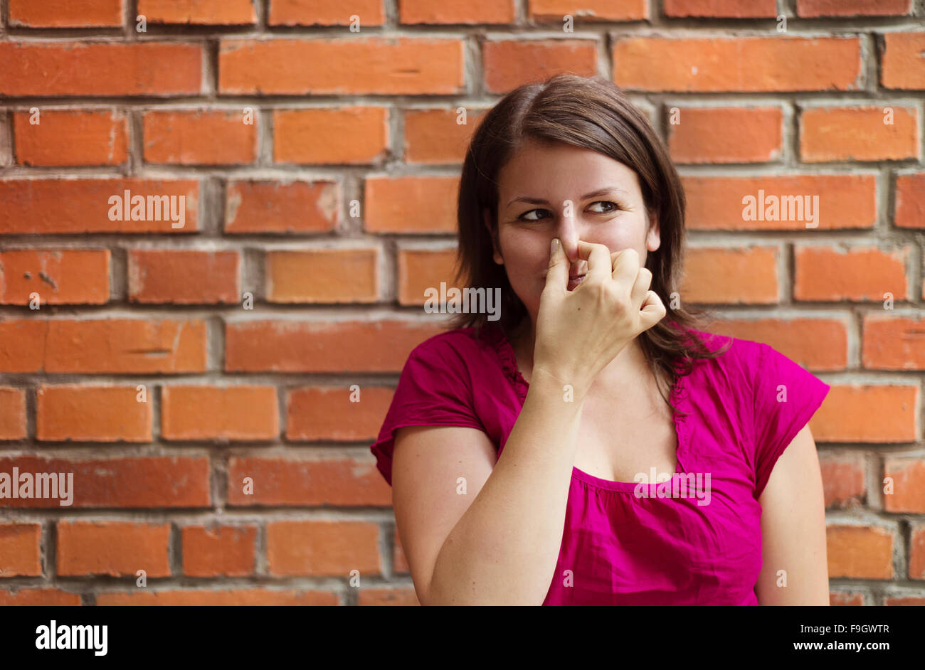 Beautiful young woman making funny faces on a brick wall background Stock Photo