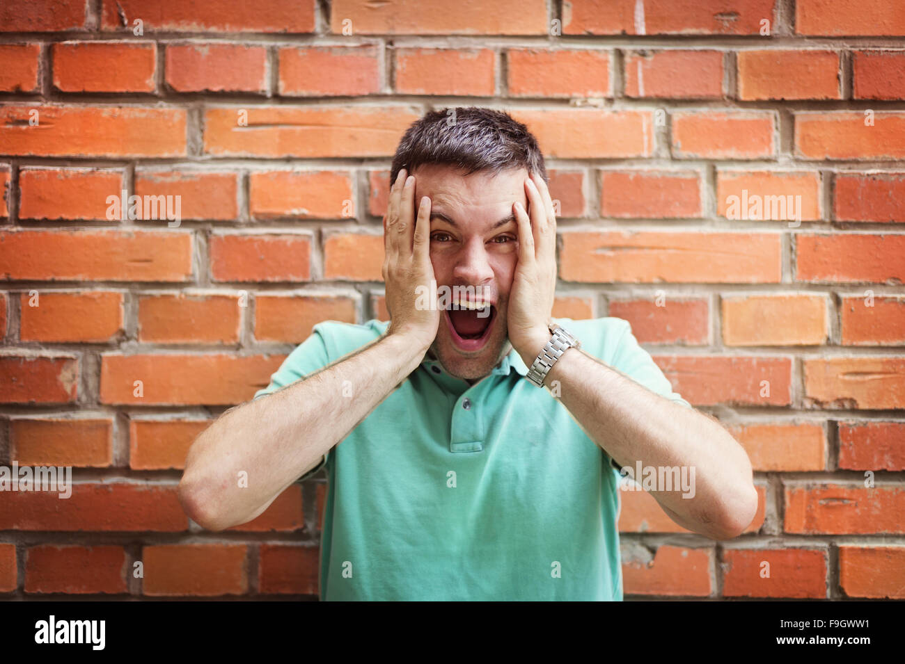 Handsome young man making funny faces on a brick wall background Stock Photo