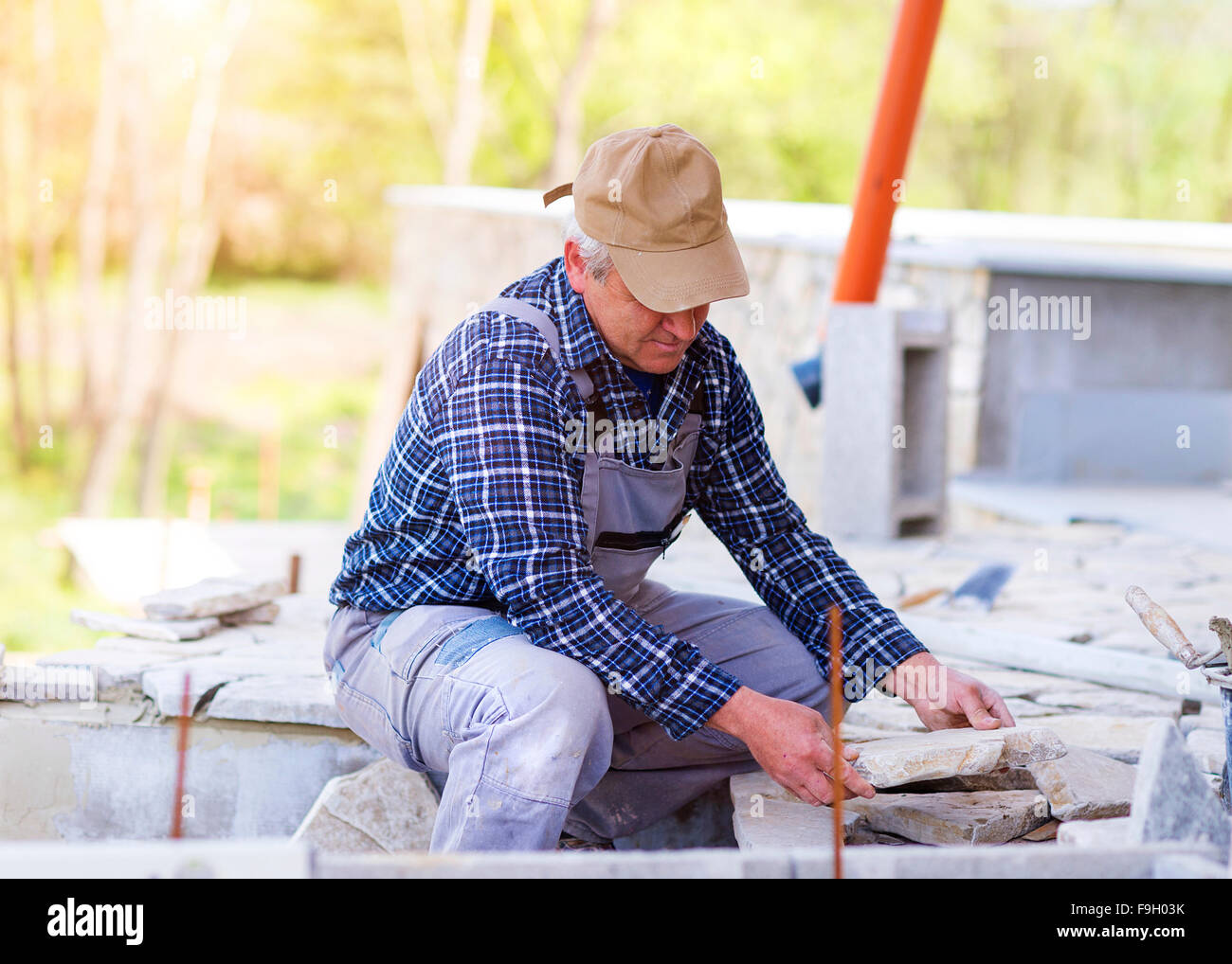 Senior man  in checked shirt laying a stone path Stock Photo