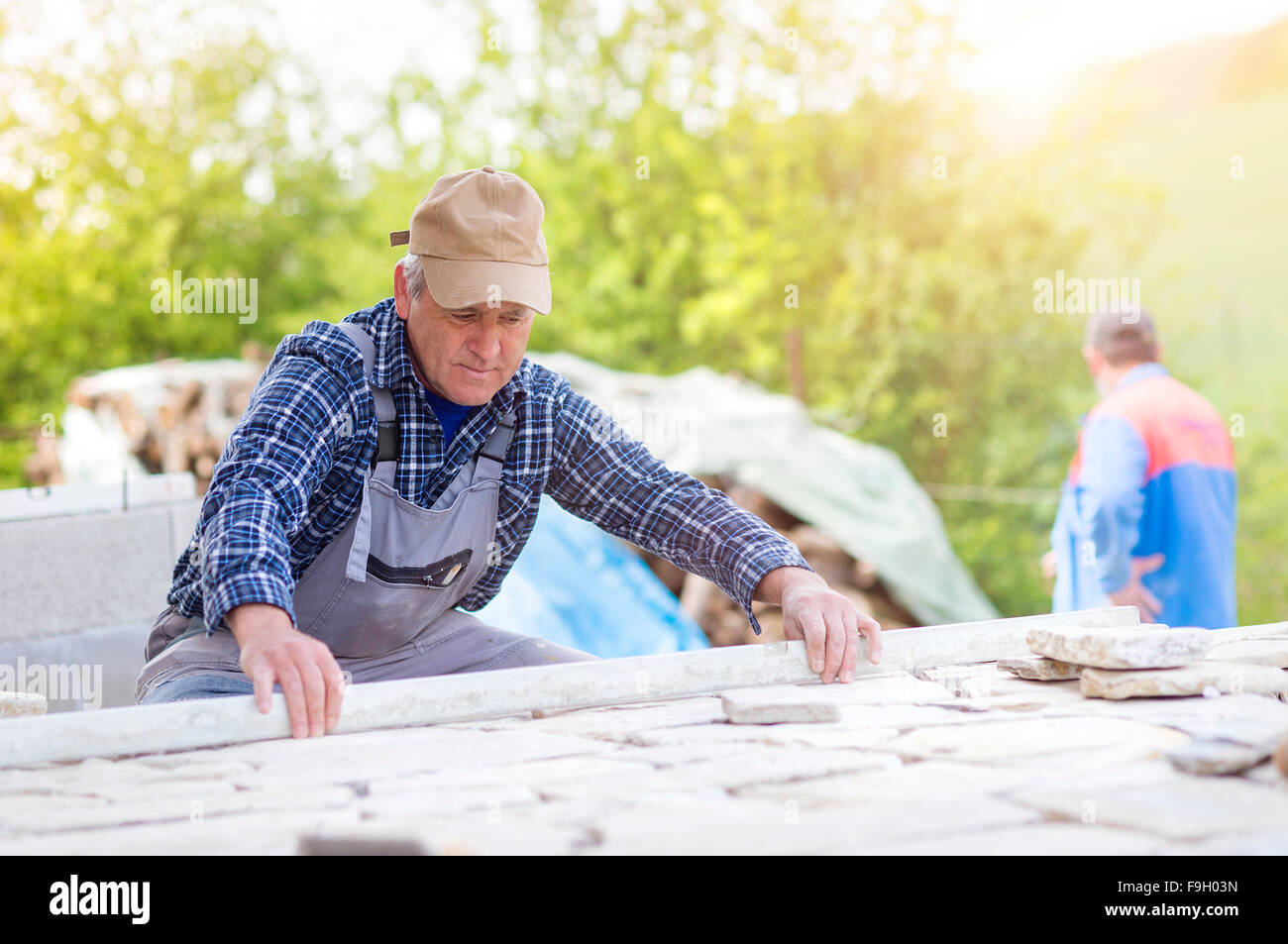 Senior man  in checked shirt laying a stone path Stock Photo