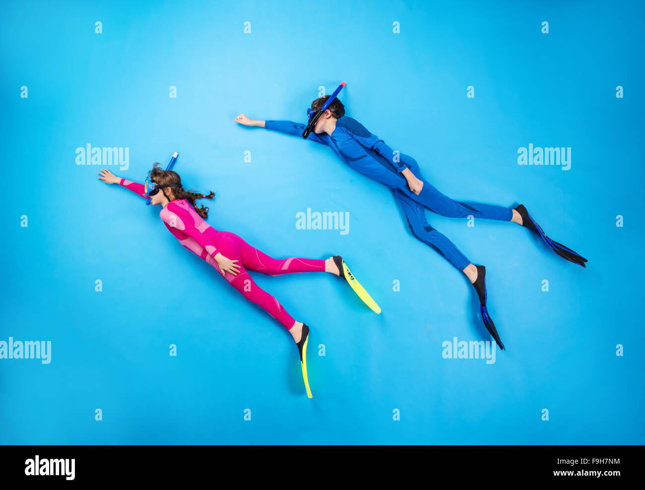 Children scuba diving deep in the sea. Studio shot on a blue background. Stock Photo