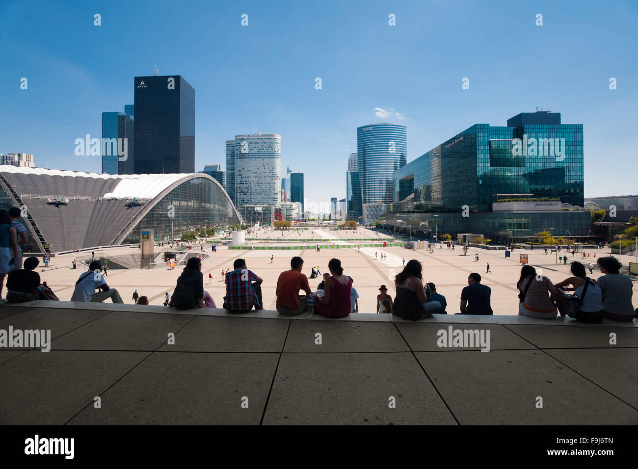 People sitting with sweeping view of the La Defense area from top steps of Grande Arche, a popular spot to relax and grab lunch Stock Photo