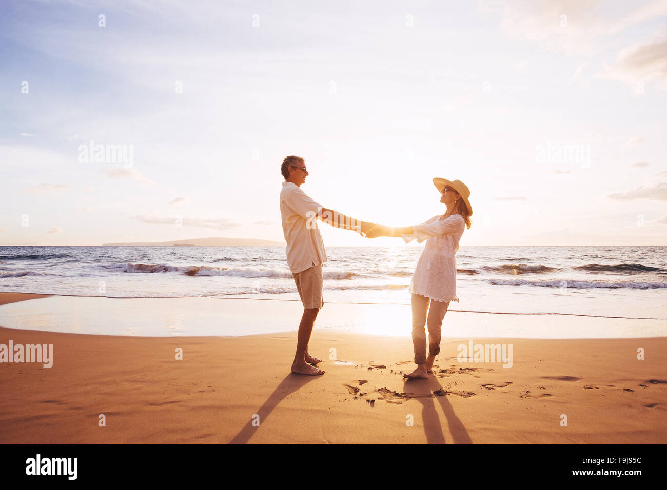 Happy Romantic Middle Aged Couple Enjoying Beautiful Sunset on the Beach. Travel Vacation Retirement Lifestyle Concept. Stock Photo