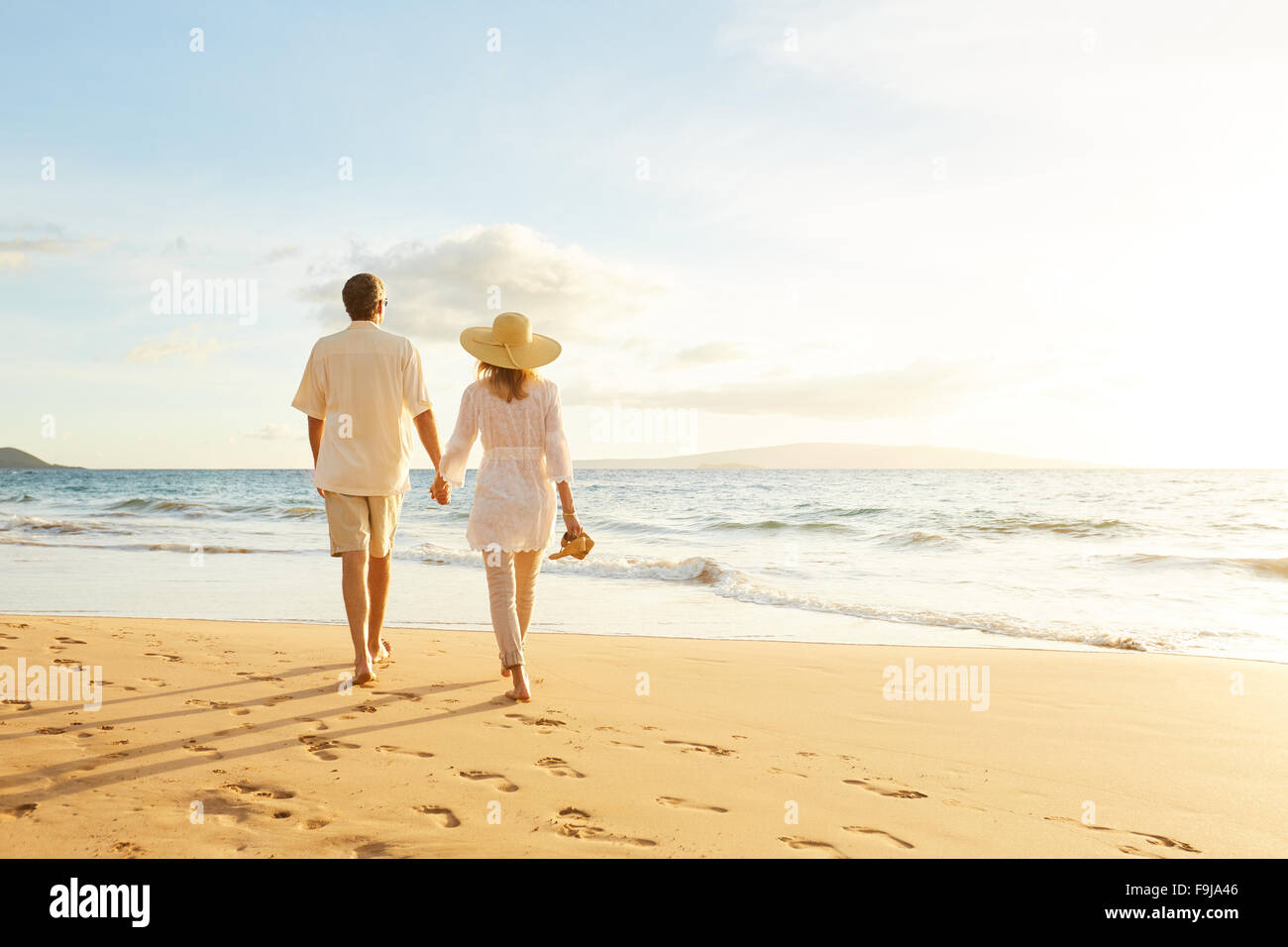 Happy Romantic Middle Aged Couple Enjoying Beautiful Sunset Walk on the Beach. Travel Vacation Retirement Lifestyle Concept Stock Photo