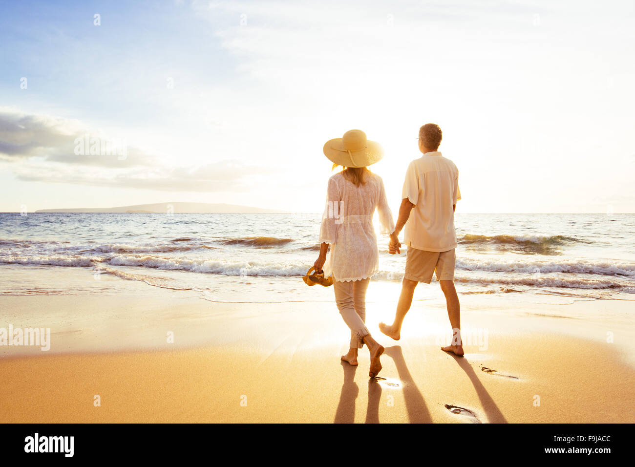 Happy Romantic Middle Aged Couple Enjoying Beautiful Sunset Walk on the Beach. Travel Vacation Retirement Lifestyle Concept Stock Photo