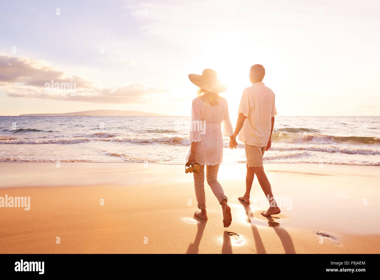 Happy Romantic Middle Aged Couple Enjoying Beautiful Sunset Walk on the Beach. Travel Vacation Retirement Lifestyle Concept Stock Photo