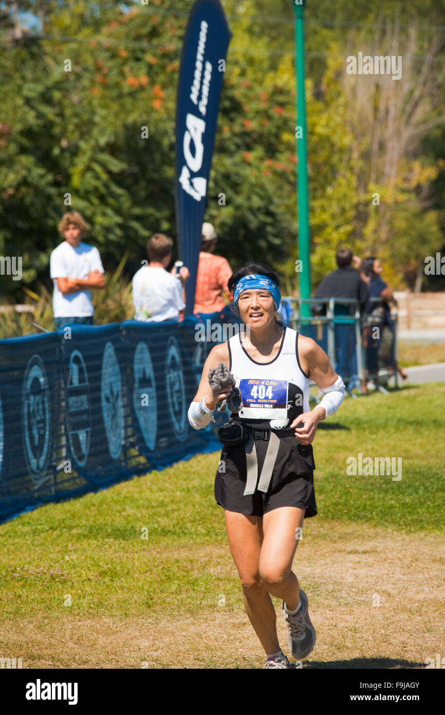 Female Asian runner crossing the finish line at the Norcal Marathon Stock Photo