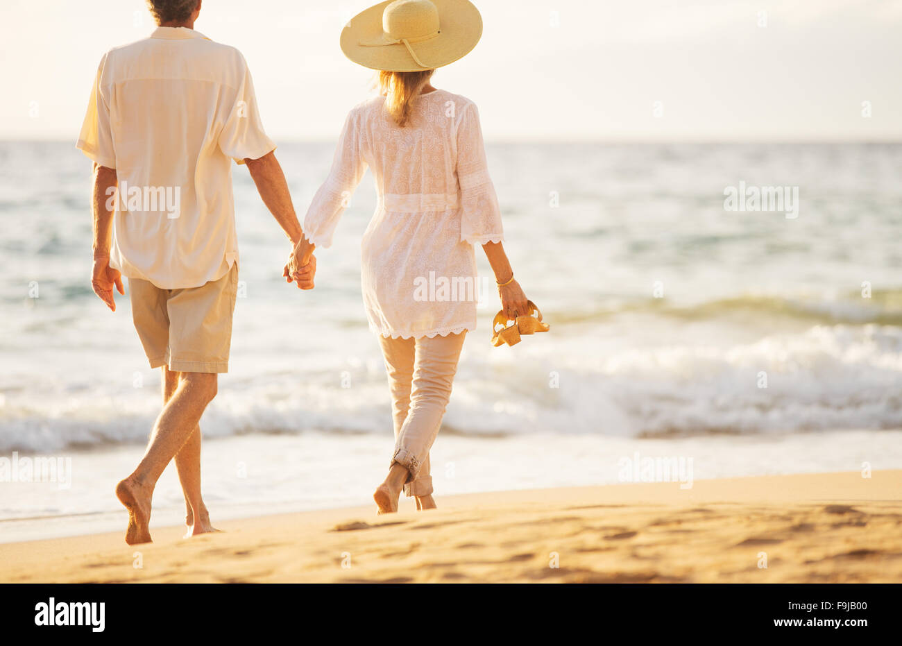Happy Romantic Middle Aged Couple Enjoying Beautiful Sunset Walk on the Beach Holding Hands Stock Photo