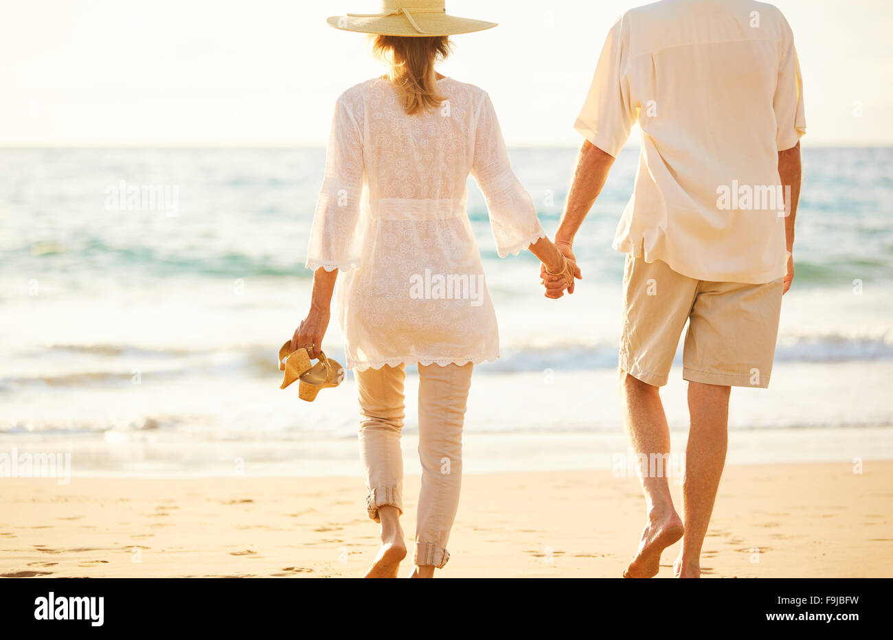 Happy Romantic Middle Aged Couple Enjoying Beautiful Sunset Walk on the Beach Holding Hands Stock Photo