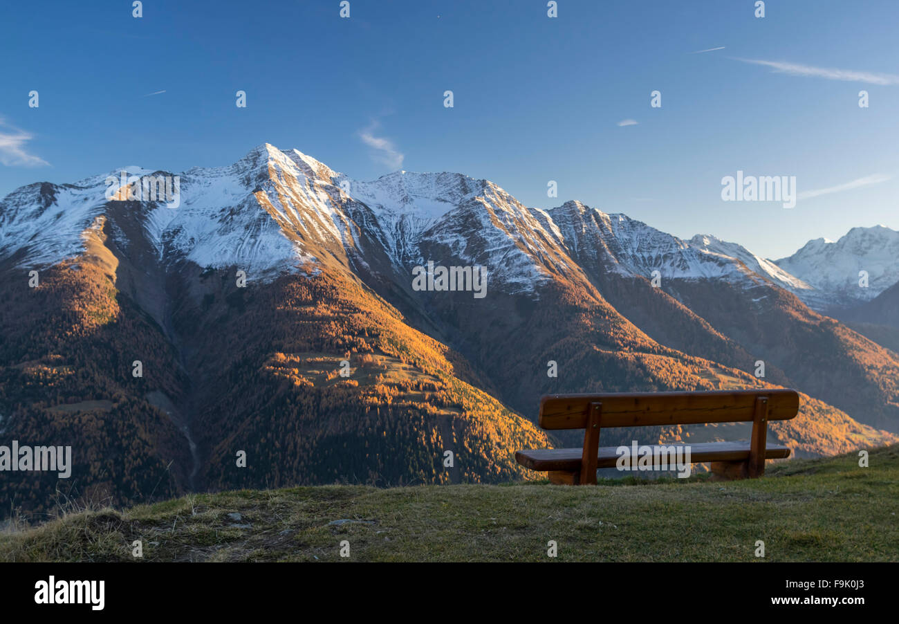 Empty bench at Bettmeralp, Valais, Switzerland with panorama of snowy mountains. Shot taken shortly before sunset. Stock Photo