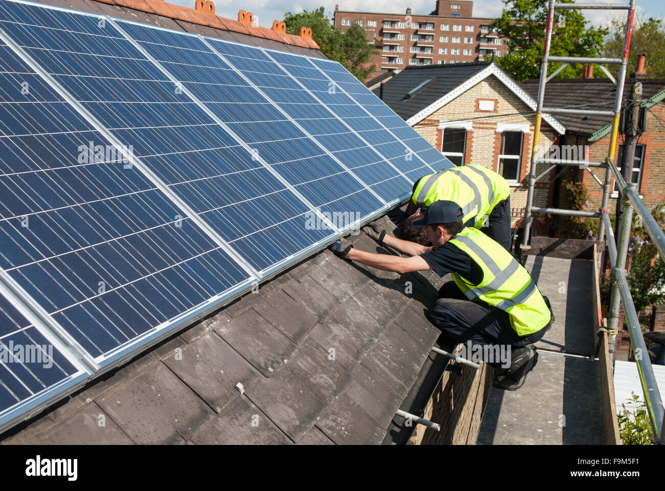 Workers install photovoltaic solar panels on the slate roof of a