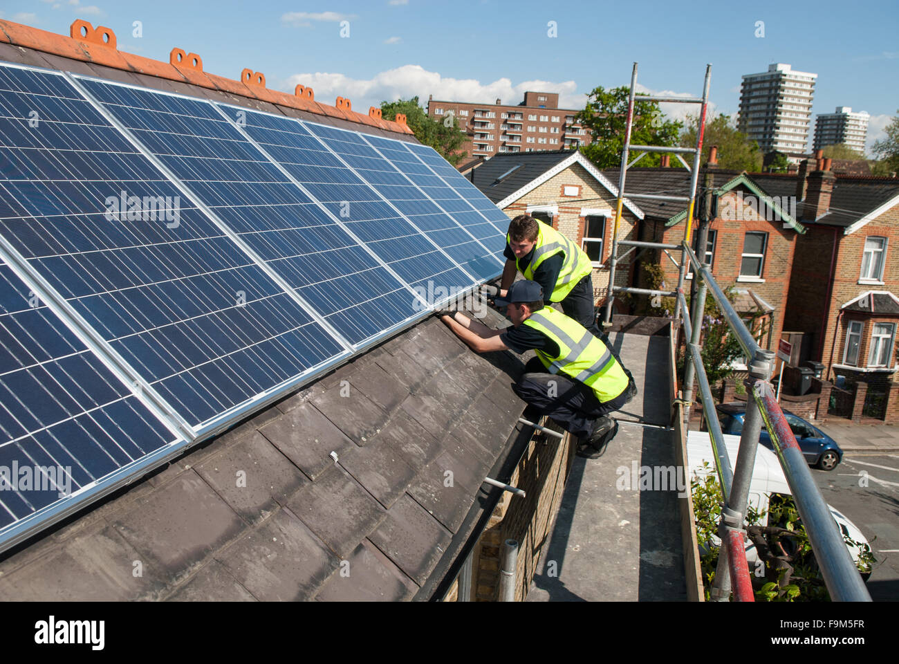 Workers install photovoltaic solar panels on the slate roof of a Victorian house in London, England. Stock Photo