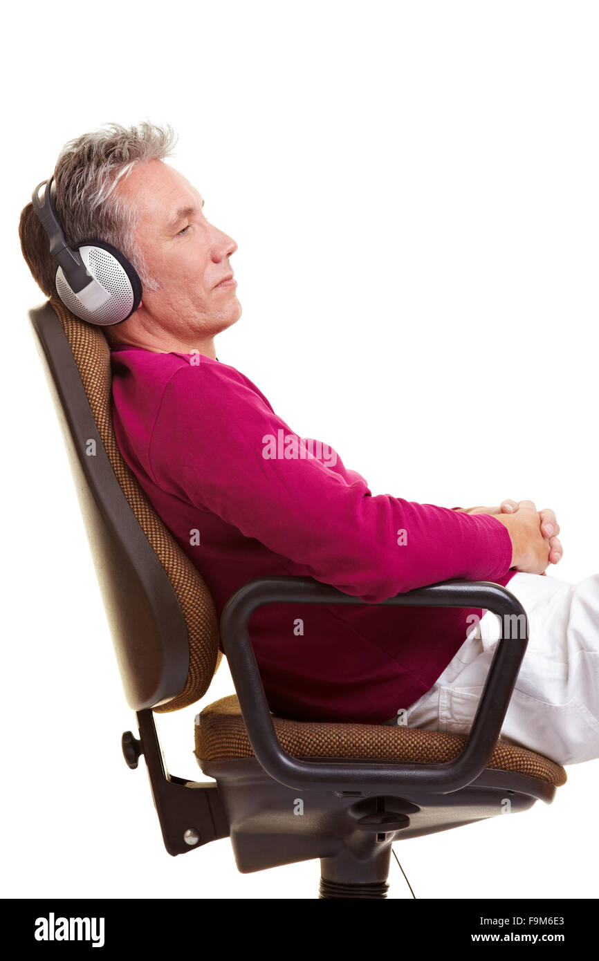 Relaxed senior man sitting on office chair and listening to music with headphones Stock Photo