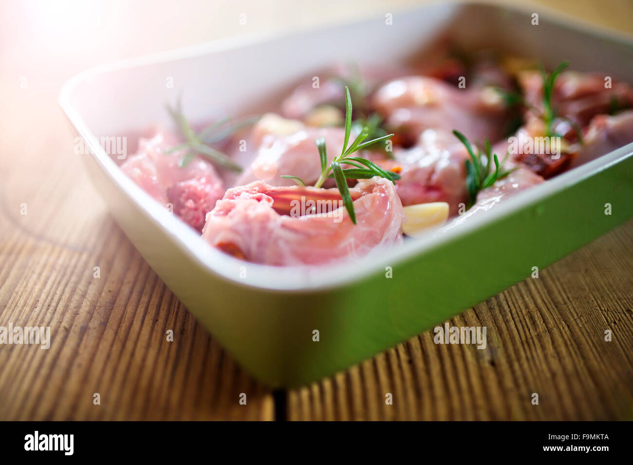 Raw fresh rabbit meat with rosemary leaves and garlic, on a green tray ready to be cooked Stock Photo