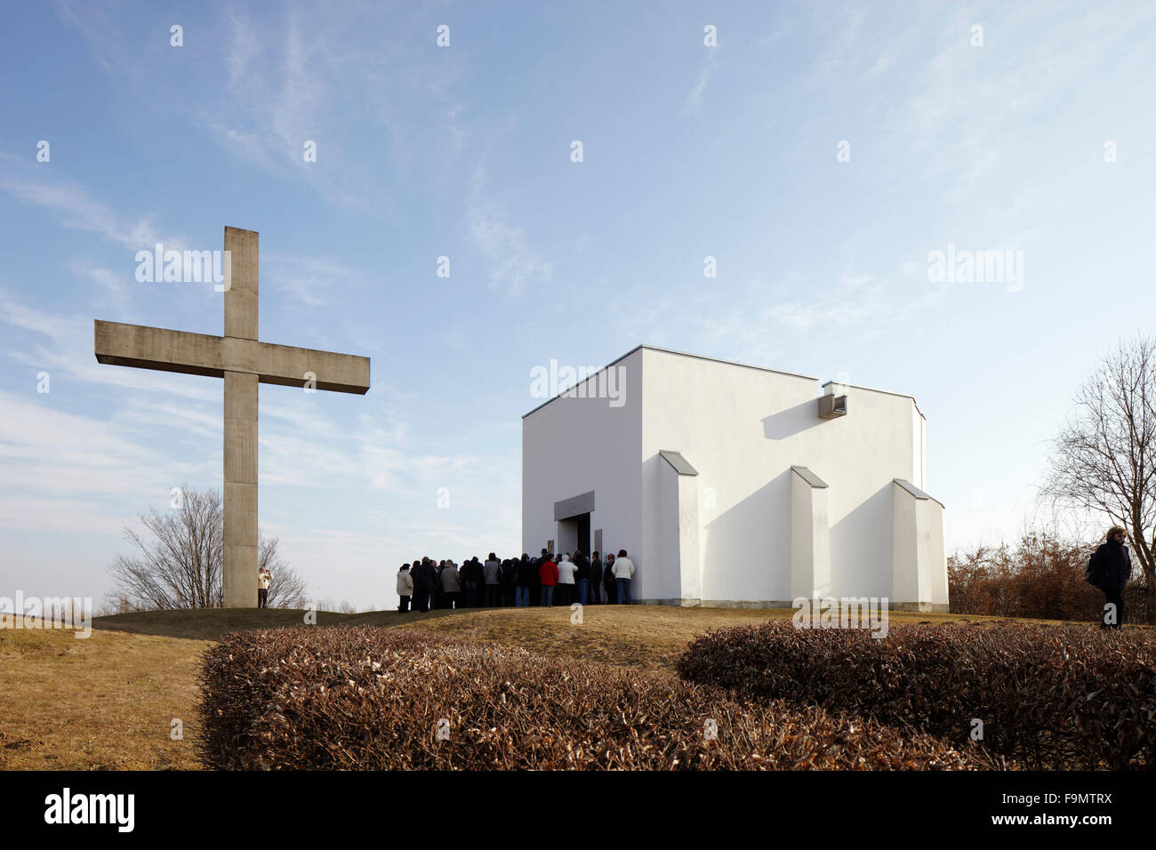 A group of people outside the Battle of Mogersdorf  Memorial Chapel and the concrete cross in the foreground at Schloesselberg near Mogersdorf, Burgenland, Austria Stock Photo