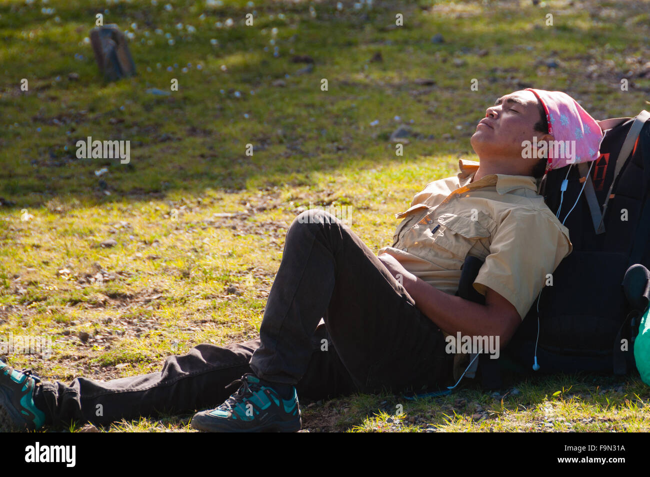 Young Man with pink bandana resting laying on his backpack in the sun