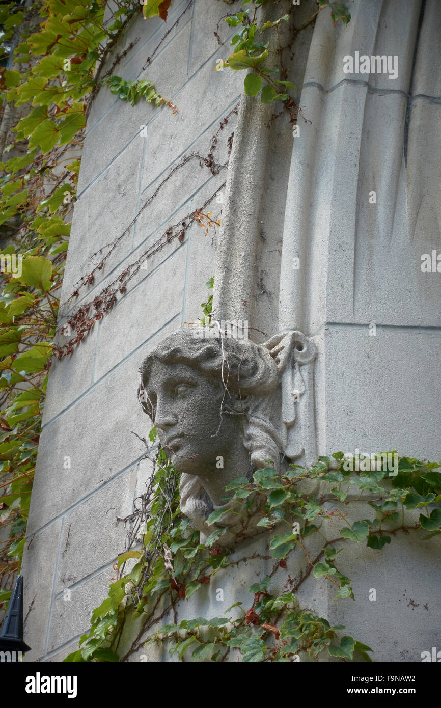 Carved sculpture of female head on building exterior surrounded with ivy Stock Photo