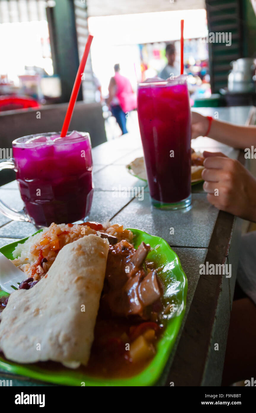 Close up of rice, bread, meat, pink drink with ice cubes and person sitting at a table in local market Leon Stock Photo