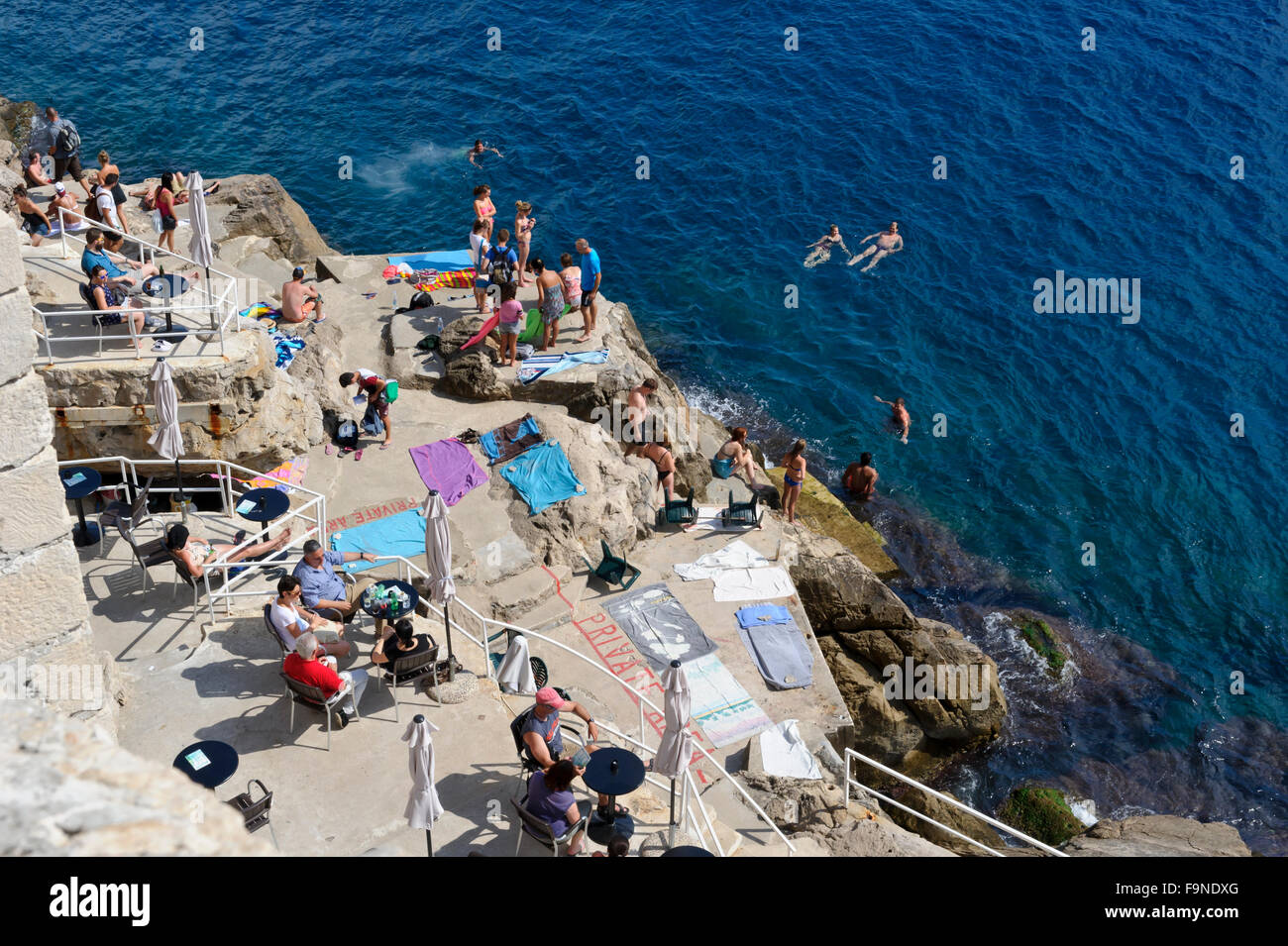 Sunbathers and swimmers at the bottom of the fortress wall, Dubrovnik, Croatia. Stock Photo