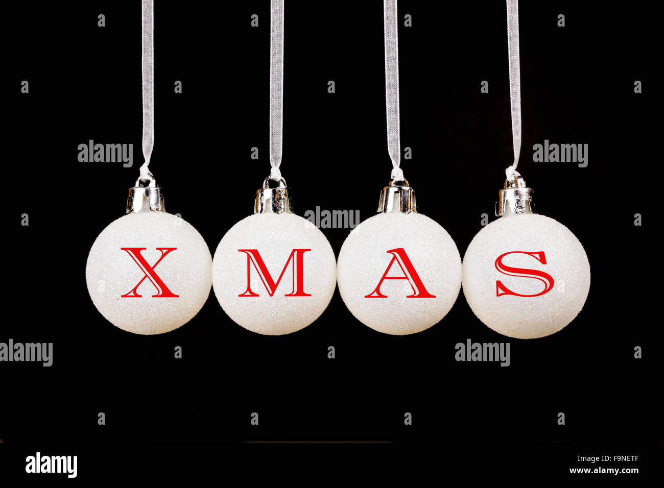 Word XMAS on white christmas balls hanging in a horizontal row isolated on black background Stock Photo
