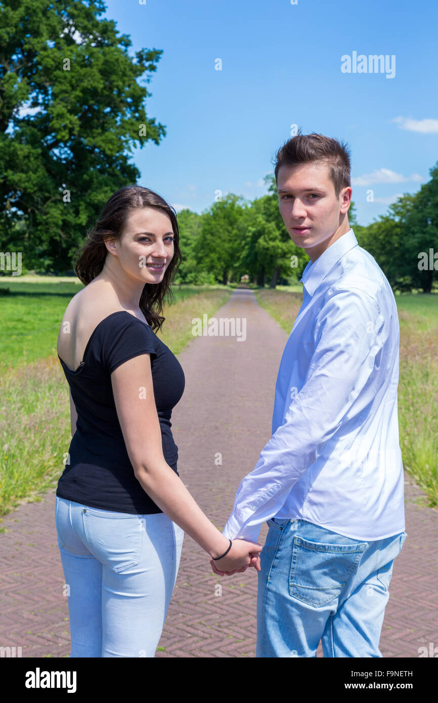 Young attractive caucasian man and woman walking hand in hand looking back Stock Photo