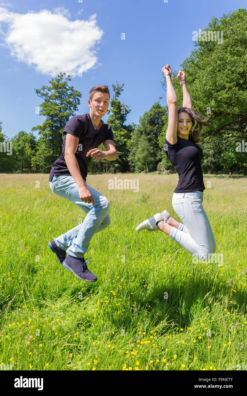 Young caucasian  man and woman  make jump in green grass on sunny day in summer Stock Photo