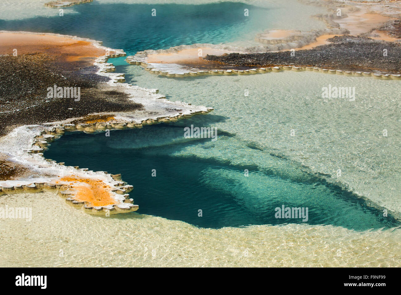 Deep aqua blue pool of a hot spring, with orange margins and foggy steam in a geothermal area of the Yellowstone caldera. Stock Photo