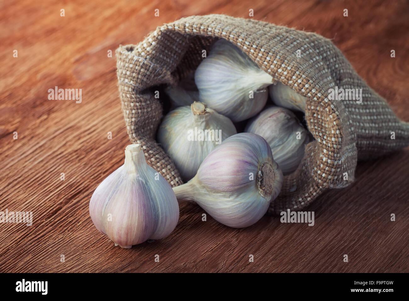 fragrant ripe garlic in a bag of coarse cloth on wooden table Stock Photo