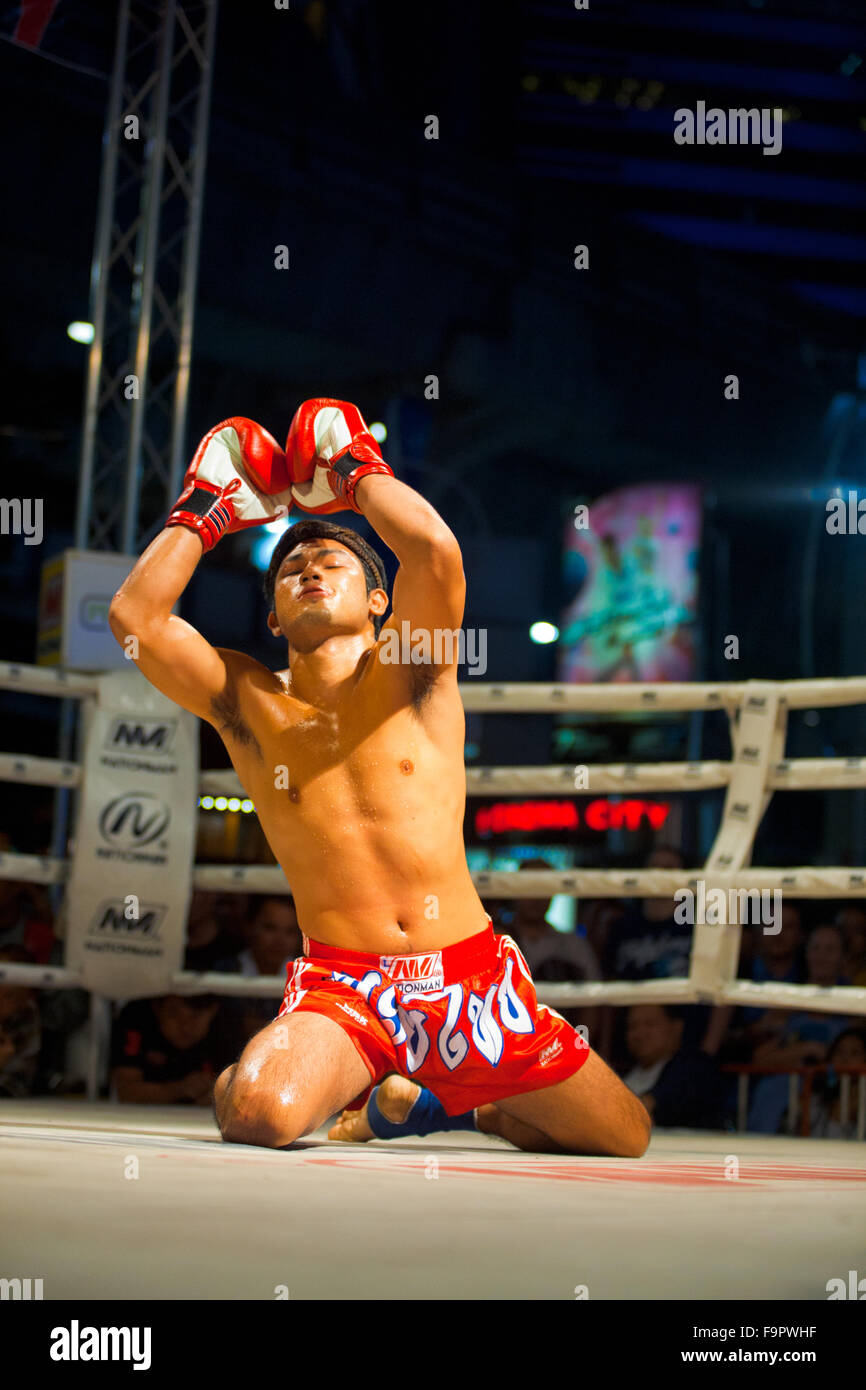 Kneeling male muay thai kickboxer in red trunks raising his arms, looking up and chanting during a traditional kickboxing ritual Stock Photo