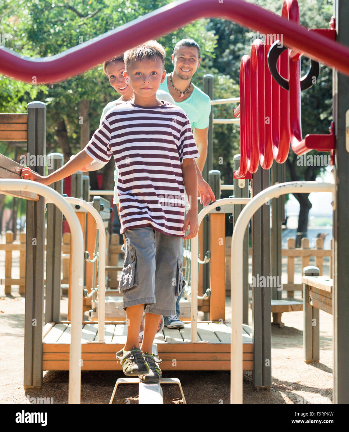 Family of three overcomes the obstacle course on the playground in summer Stock Photo