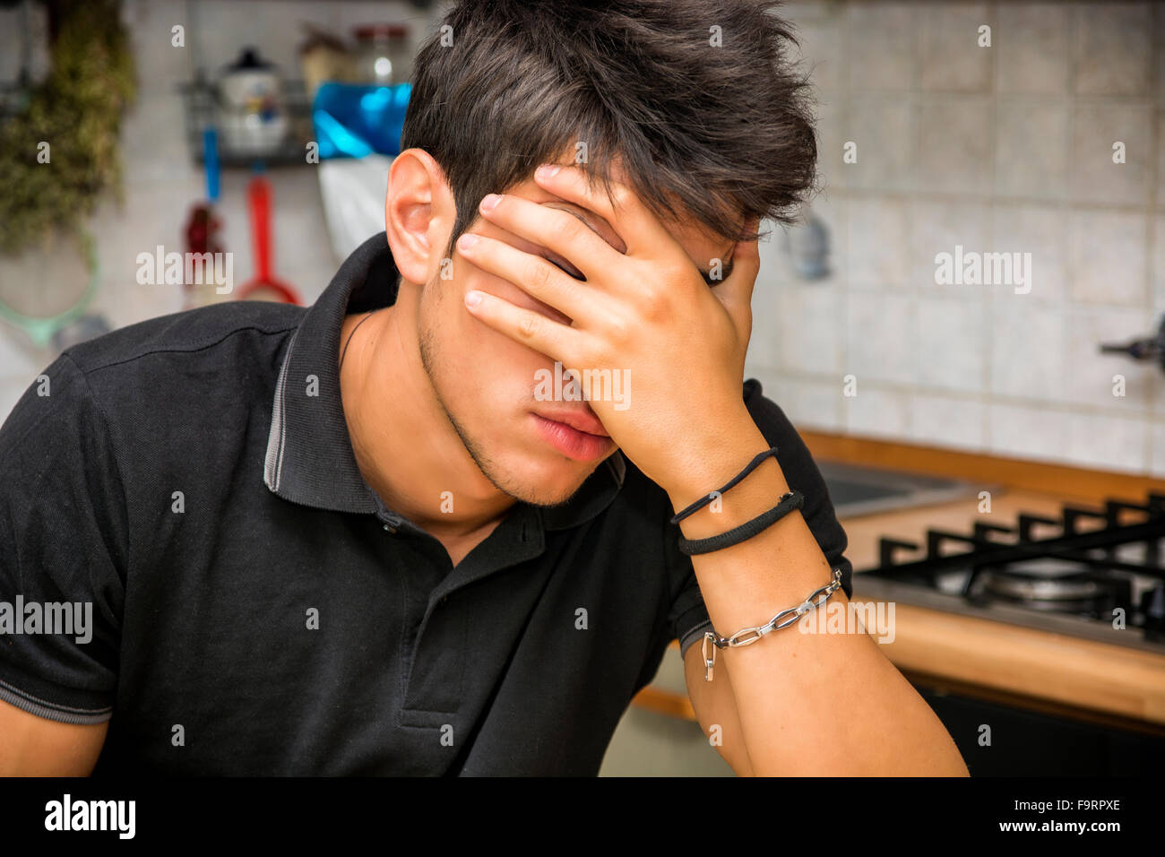 Depressed man hiding face with hand while sitting in the kitchen Stock Photo