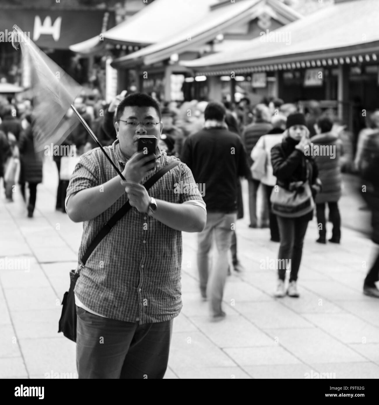 A male tour guide waits, his flag fluttering, for his tour at the Sensō-ji temple (金龍山浅草寺) in Asakusa, Tokyo. Stock Photo