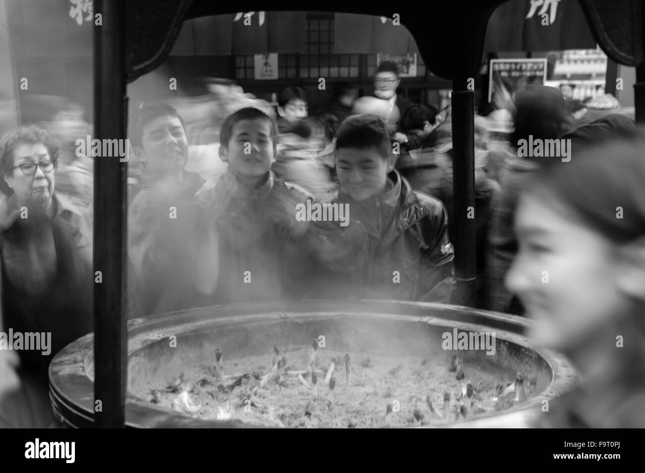 Three boys visiting the Sensō-ji temple (金龍山浅草寺) in Asakusa, Tokyo, wafting incense smoke over themselves. Stock Photo