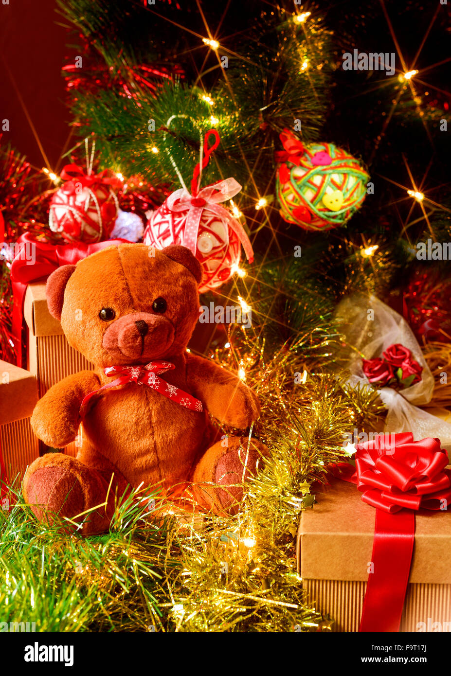 closeup of a brown teddy bear and some gifts under a christmas tree ornamented with lights, balls and tinsel Stock Photo