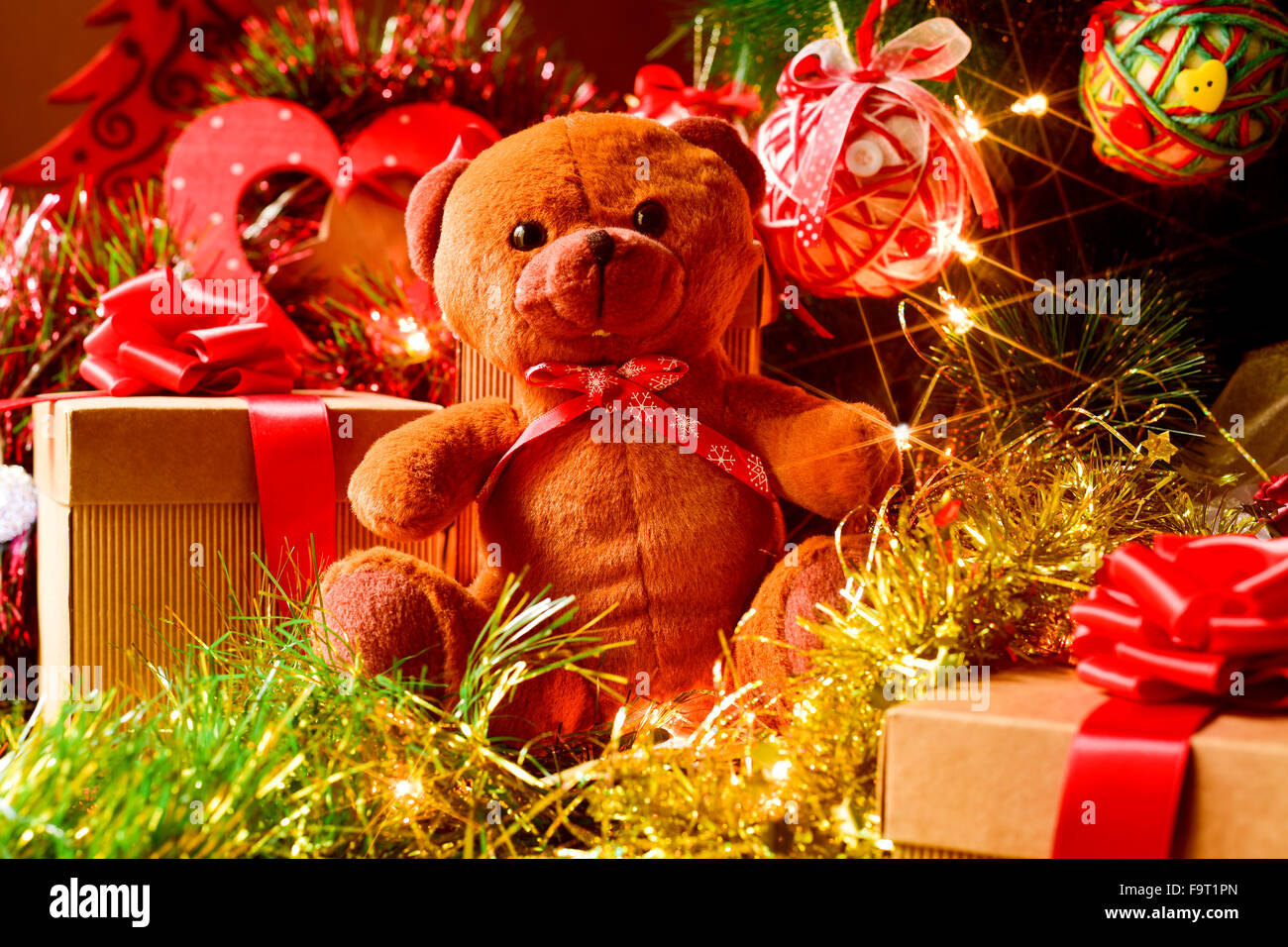 closeup of a brown teddy bear and some gifts under a christmas tree ornamented with lights, balls and tinsel Stock Photo