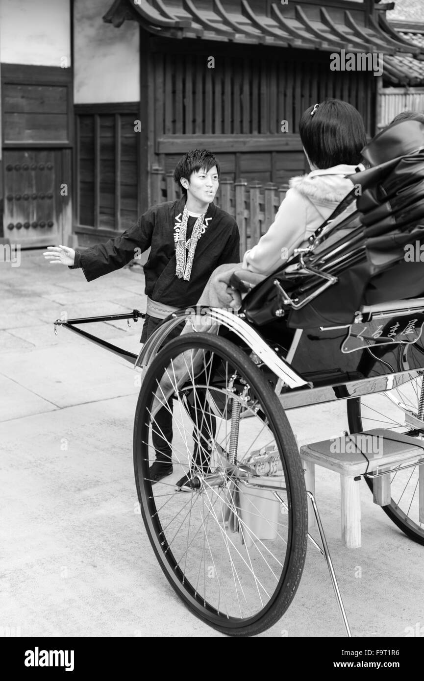 A male tour guide and rickshaw driver at the Sensō-ji temple (金龍山浅草寺) in Asakusa, Tokyo, showing a temple gate to a couple. Stock Photo