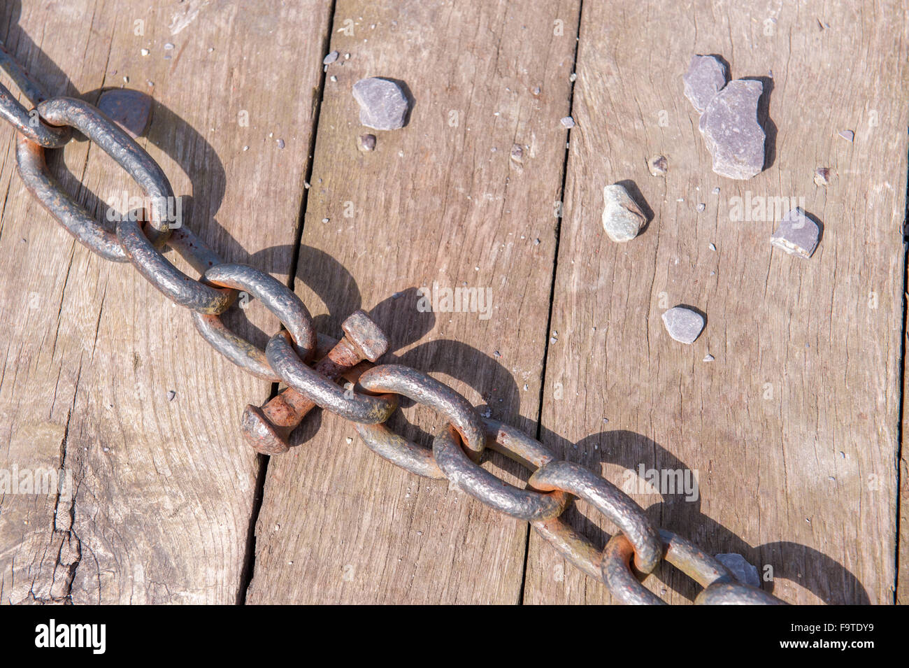 Metal linked chain on wooden surface and bolt Stock Photo