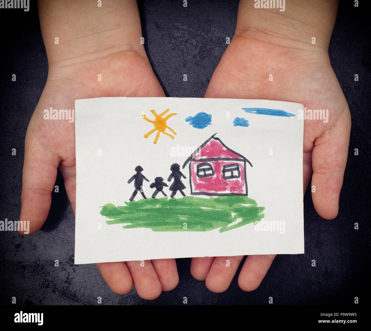 Child holds a drawn house with family. Close up. Stock Photo