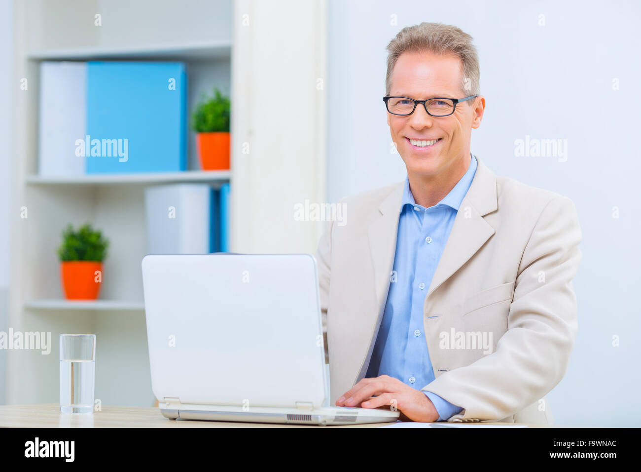 Smiling businessman sitting at his desk Stock Photo - Alamy