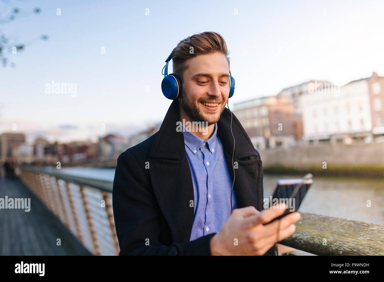Ireland, Dublin, young man holding smartphone hearing music with