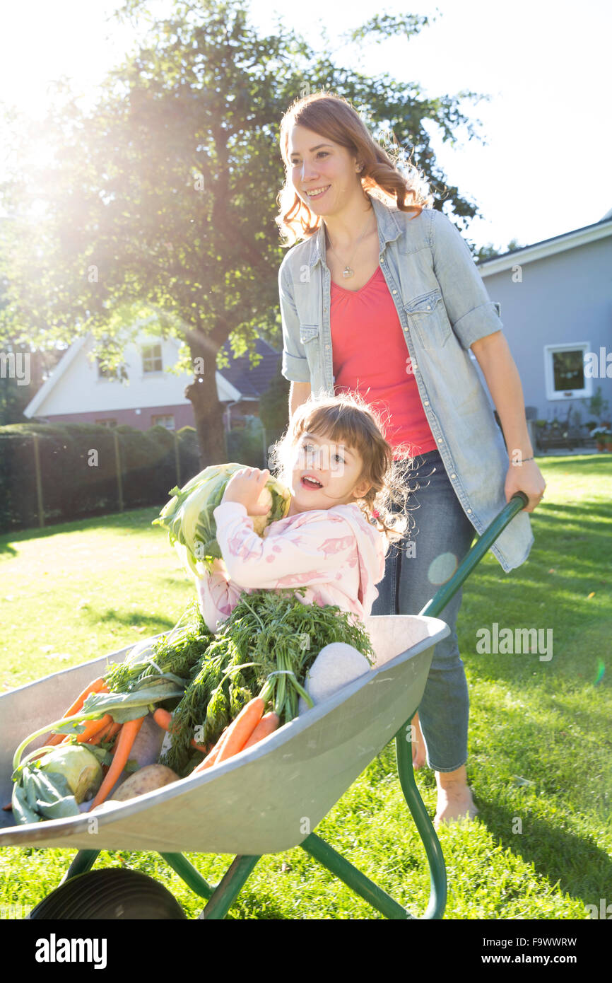 Mother pushing daughter with vegetables in wheelbarrow in garden Stock ...