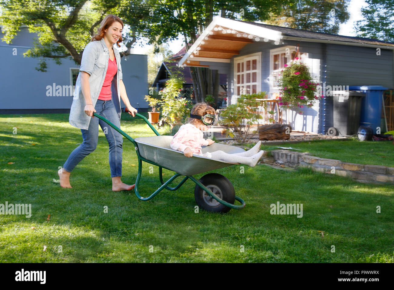 Mother having fun with daughter in wheelbarrow in garden Stock Photo ...