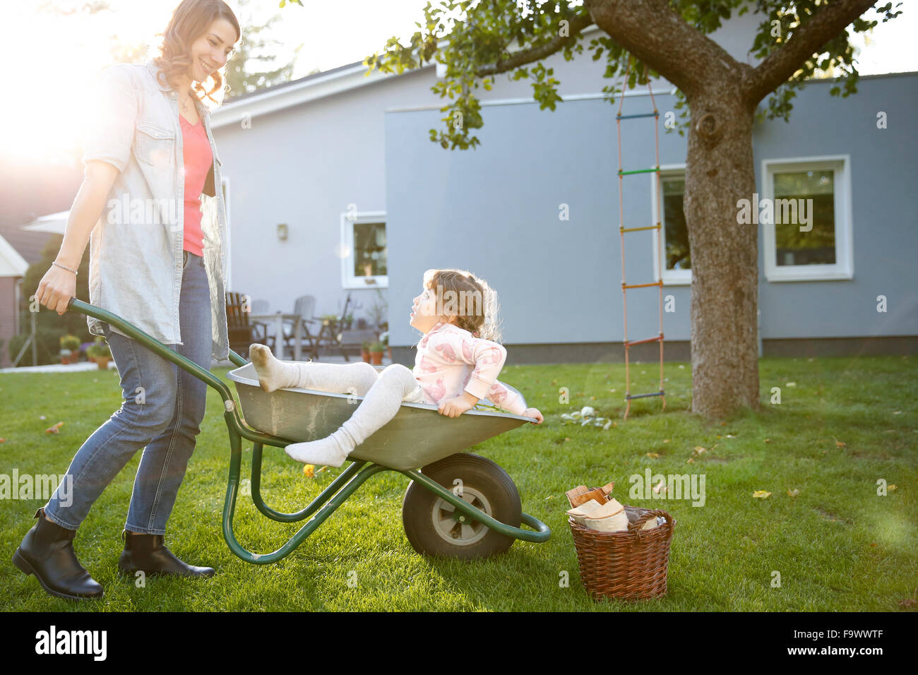 Mother pushing daughter in wheelbarrow in garden Stock Photo - Alamy