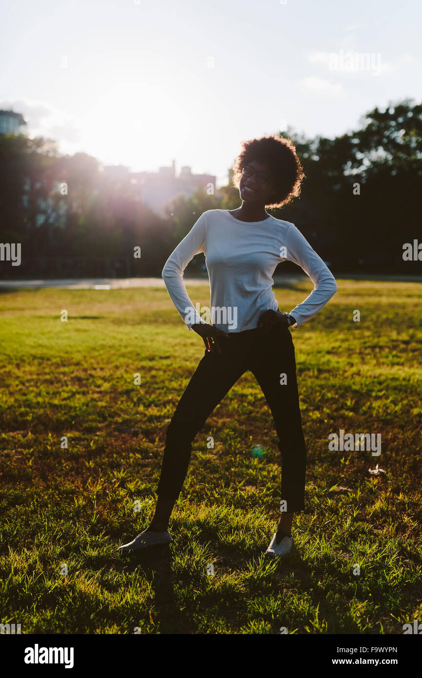 Smiling young woman standing with hands on her hips on a meadow of a ...