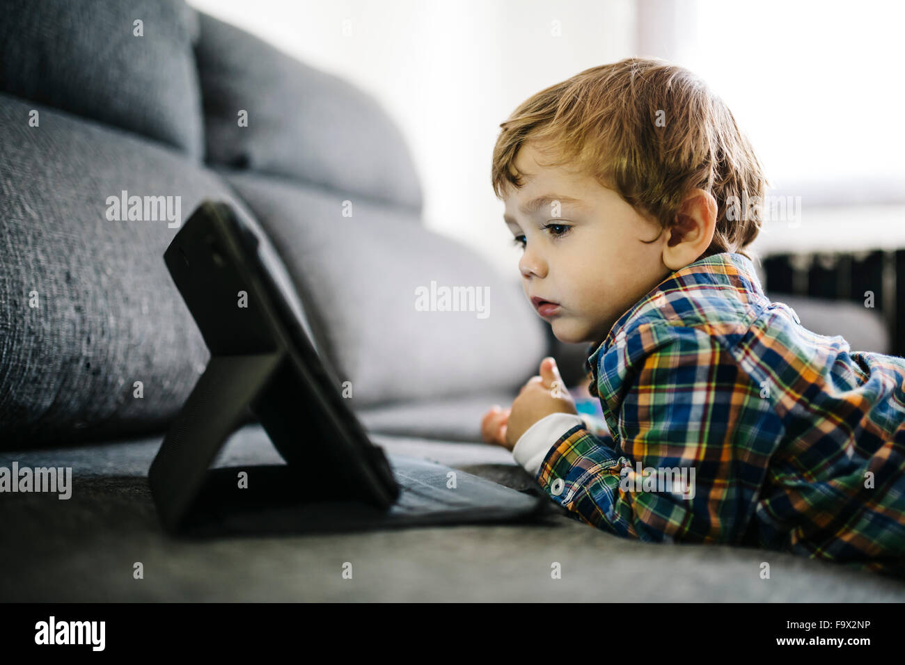 Portrait of little boy lying on the couch looking at digital tablet ...
