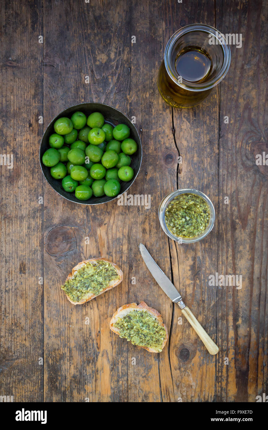 Bowl of green olives, carafe with olive oil, knife and slices of bread