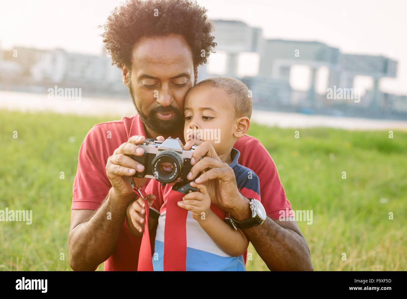 Germany, Cologne, father explaining camera to his son in a field Stock Photo