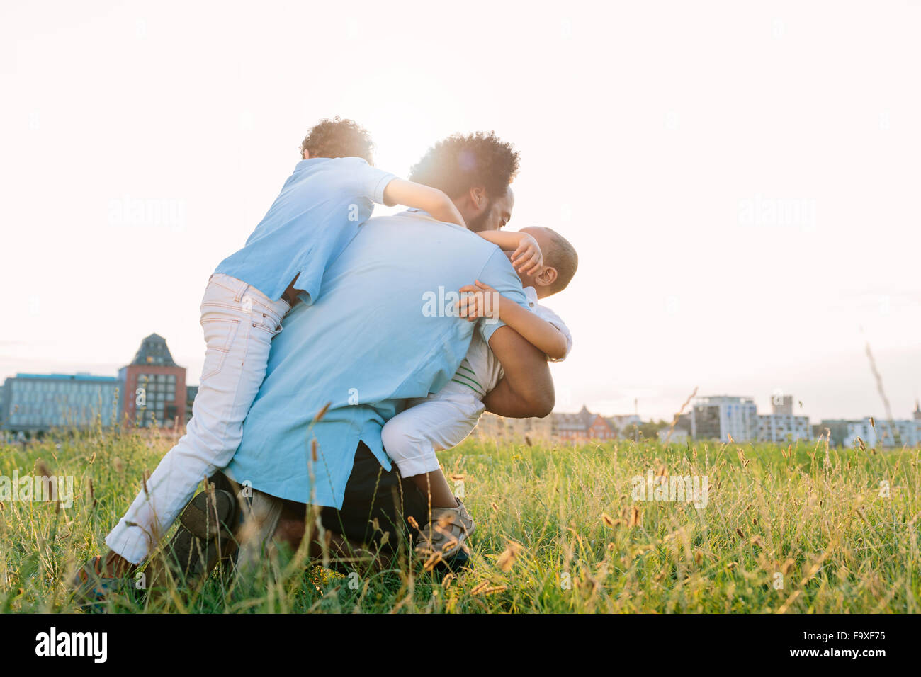 Germany, Cologne, playful father with two sons in field Stock Photo