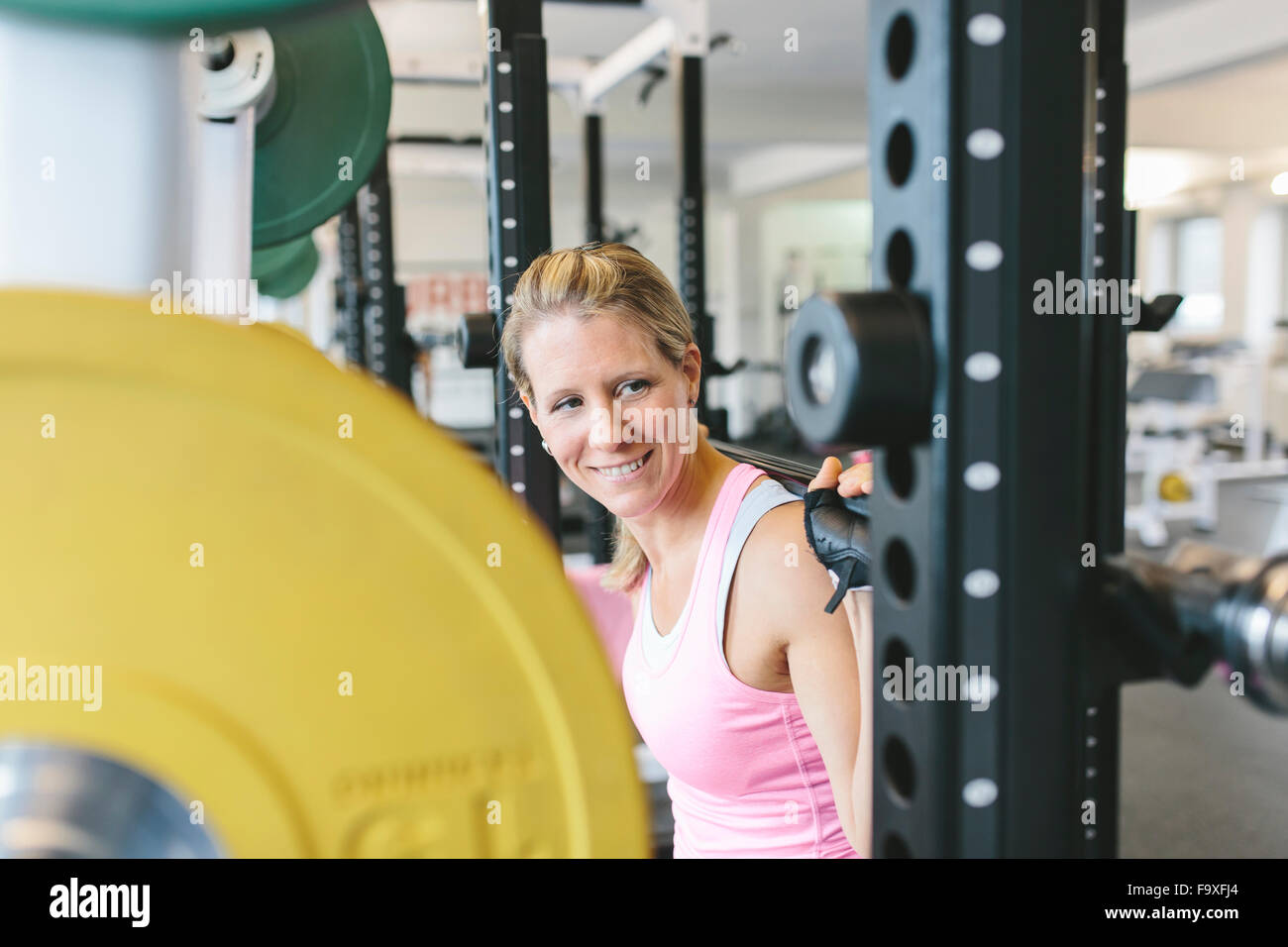 Smiling woman doing barbell squats in a power rack Stock Photo